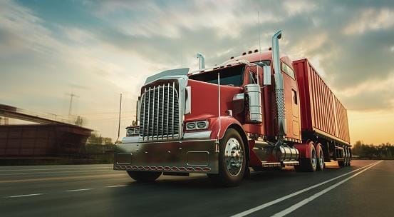 A red semi-truck with a large trailer, driven by a professional truck driver, glides down the highway at sunset, embodying due care and commitment to a higher standard.