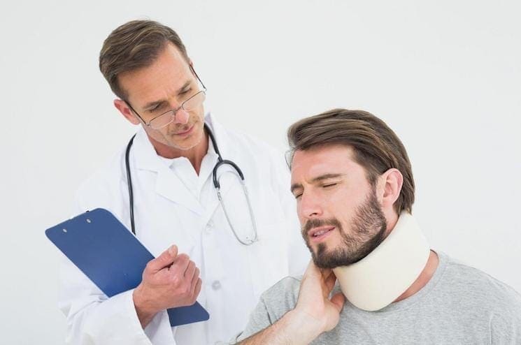 A doctor with a clipboard conducts an Independent Medical Examination on a man wearing a neck brace, who is gently touching his neck.