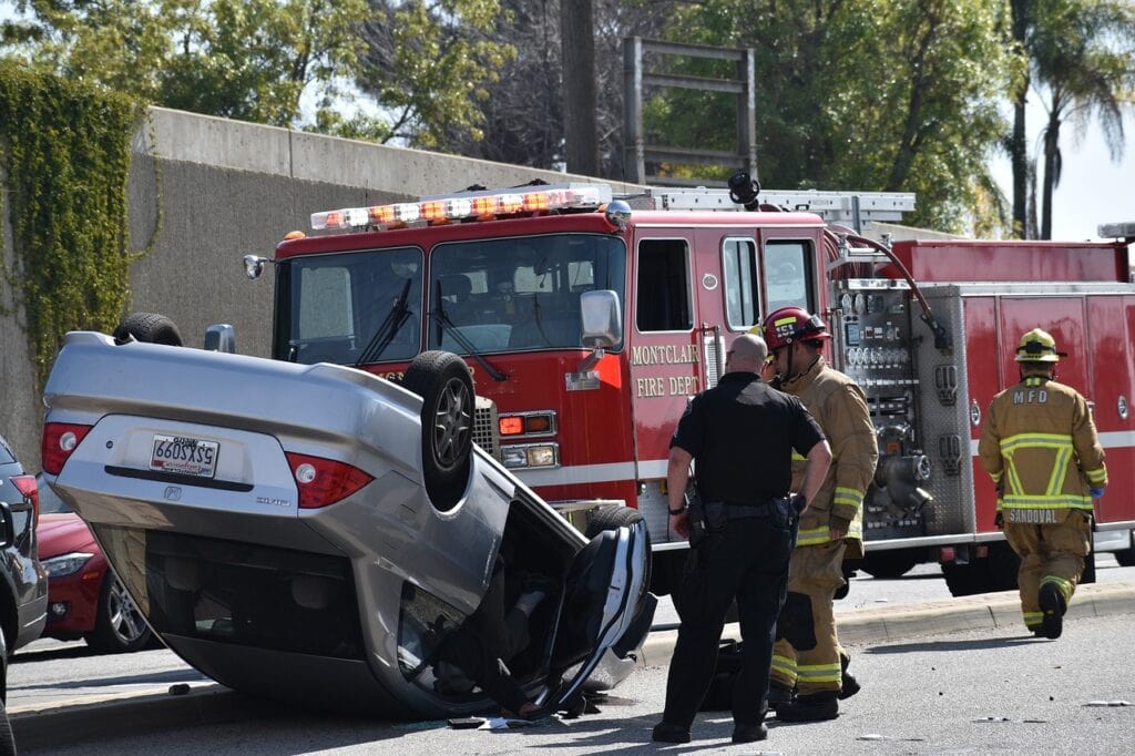 Firefighters and police officers are diligently working at the scene of an overturned car accident, with a fire truck stationed in the background. In such situations, consulting a rollover accident lawyer can be crucial for understanding your rights and seeking justice.