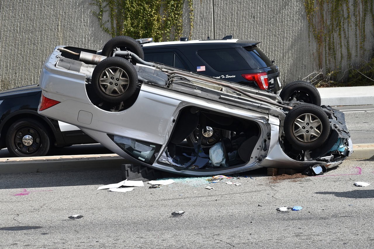 Overturned silver car on a road, surrounded by debris, with a police vehicle nearby—an all-too-familiar scene for a rollover accident lawyer.