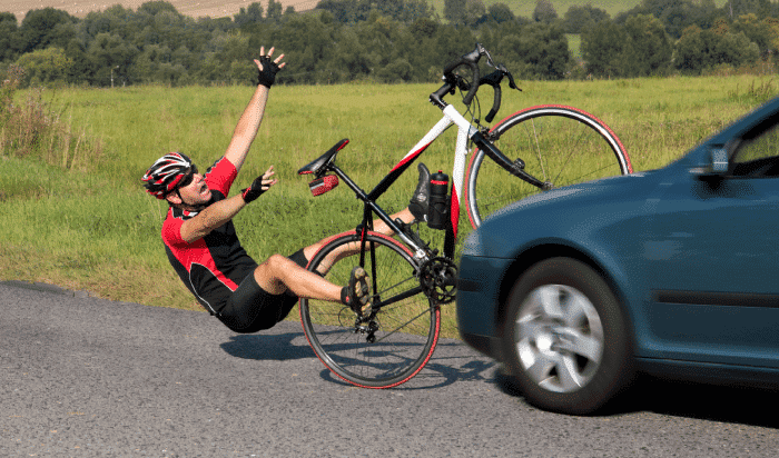 Cyclist in red and black gear involved in a bike accident as a car passes by on a rural Michigan road.