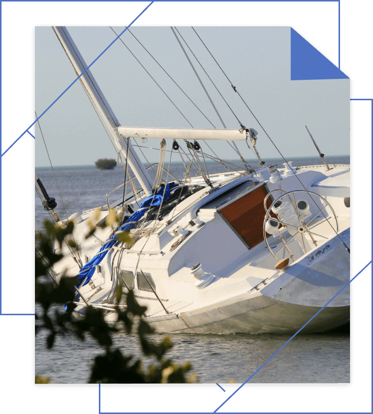 The sailboat tipped over in shallow water near a small tree-covered islet, its mast leaning and deck partially submerged. If you need legal help for boating accidents in Michigan, reaching out to an experienced boat accident lawyer can make navigating claims smoother.
