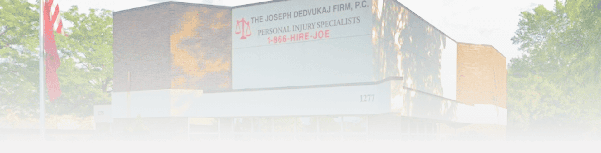 Exterior view of a law firm's building with signage for personal injury specialists and a phone number. Trees and a flagpole are visible outside.