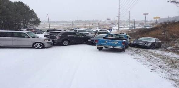 A minor pile-up has occurred on a snowy road, involving multiple vehicles, some parked on the roadside. Snow blankets the ground and trees, painting a clear picture of winter conditions.