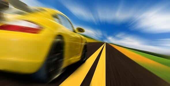A yellow sports car, pushing the limits of excessive speed, zooms down the road with motion blur against a backdrop of blue sky and clouds.
