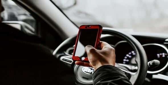 Seated in a car's driver's seat, a person clutches a red smartphone, hinting at the potential consequences of distracted driving in Michigan as the steering wheel looms in the background.