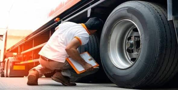 A person meticulously inspects a truck's tires with a clipboard in hand, ensuring every detail is noted. This thorough examination helps prevent any potential accidents that could arise from negligent inspection.
