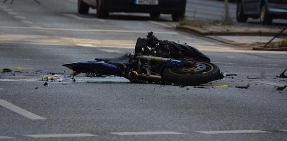 A motorcycle lies on its side in the middle of a road, appearing damaged after an accident—a stark reminder of the importance of motorcycle safety. Debris is scattered around the site.