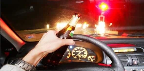 A person grips a beer bottle while driving at night, with blurred traffic lights streaming through the windshield—a risky scene that underscores the need for accident attorneys after an alcohol-related driving incident.