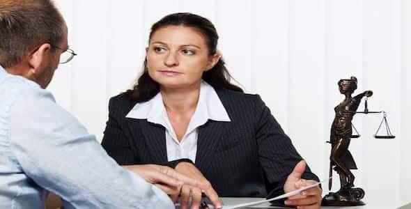 A woman in a suit talks seriously with a man seated opposite her, delving into the intricacies of wrongful death cases. A statue of Lady Justice stands as a silent witness on the table, underscoring their commitment to justice in Michigan.