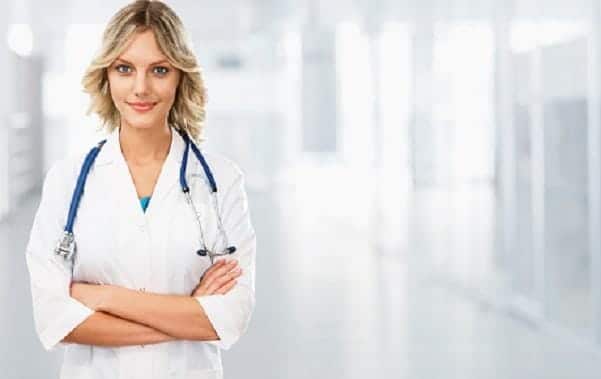 Person in a white lab coat with a stethoscope around their neck, standing with arms crossed in a bright, blurry corridor, ready to discuss telemedicine innovations.