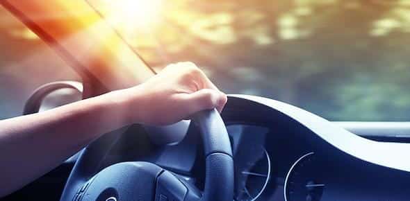 A hand grips the steering wheel in a moving car, with sunlight streaming through the window, unaware of an imminent car accident.