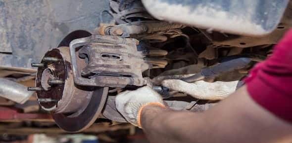 A person wearing gloves is meticulously working on a truck's brake system in Michigan, focusing on the caliper and rotor to prevent mechanical failure.