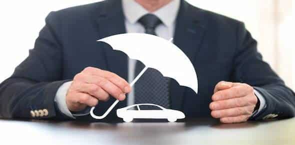 A person in a suit holds a cutout of a white umbrella over a white car model on a table, symbolizing Michigan auto insurance and protection for savvy auto insurance buyers.