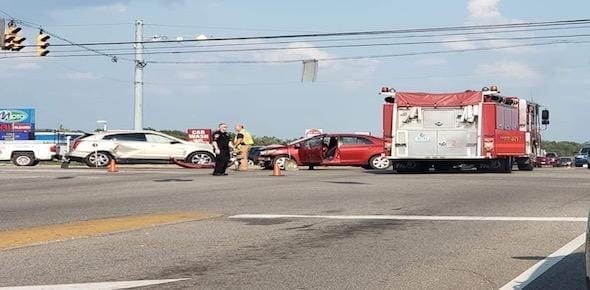 At the intersection accident scene, a red car and a white SUV are visibly damaged alongside a fire truck. Emergency personnel attend to those hurt in the wreck, ensuring safety and assessing personal injuries.