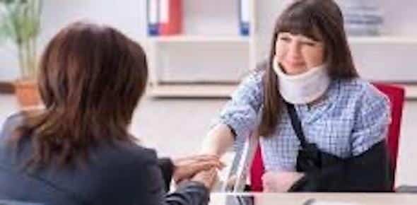 A woman with a neck brace and arm sling sits at a desk, holding hands with another seated woman, perhaps discussing the FAQs about car accidents to understand her situation better.