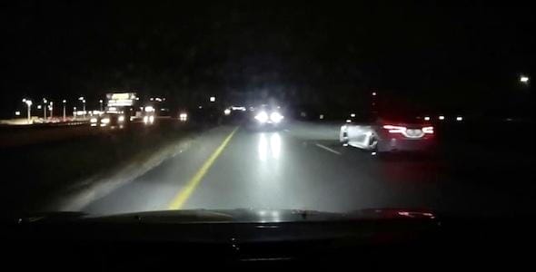 Nighttime highway scene in Michigan with cars driving in opposite directions. The road, illuminated by headlights, has roadside lights visible in the background. Remember safety tips to avoid being a wrong way driver on these bustling roads.
