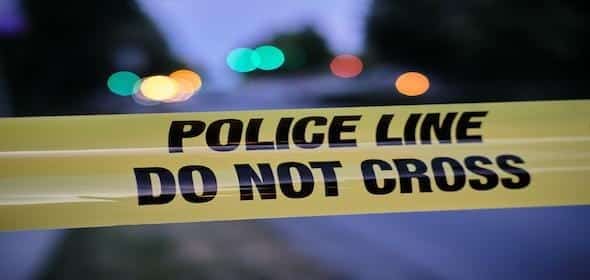 Yellow police tape with "POLICE LINE DO NOT CROSS" text; blurred lights in the background hinting at a Michigan scene under investigation tied to a potential wrongful death case.