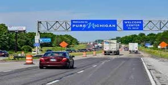 Cars and trucks travel on a highway beneath a sign reading "Welcome to Pure Michigan," with traffic cones along the road reminding drivers about safe stopping distances to enhance car safety.