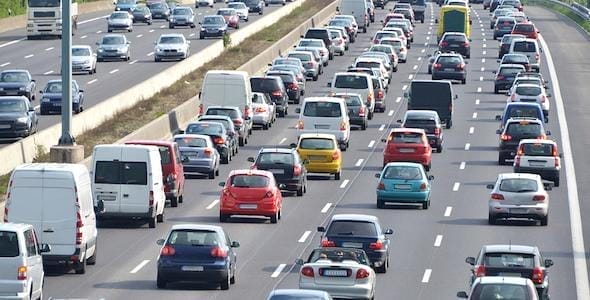 Heavy traffic on a multi-lane highway with cars, vans, and trucks traveling in both directions under clear skies, as authorities issue a ticket to an at-fault driver following a Michigan car accident.