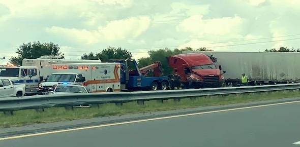 A red semi-truck and trailer lie involved in a roadside accident, with emergency vehicles like an ambulance and police car attending the scene. If you're hurt in truck accidents, it's crucial to know what steps to take next for your safety and legal rights.
