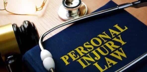 Close-up of a book titled "Personal Injury Law" with a stethoscope, a gavel, and glasses resting on a wooden surface, illustrating the essential tools in navigating the basic stages of a Michigan personal injury lawsuit.