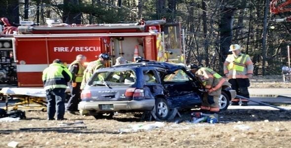 Emergency responders are at the scene of an angle collision car accident involving a blue vehicle and a fire rescue truck in a wooded area.