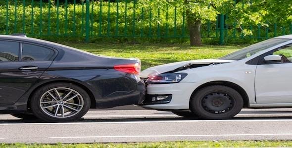 A black car and a white car are involved in a rear-end collision on the road, with minor damage visible to both vehicles. The incident raises questions about driving responsibility and which driver might be at fault.