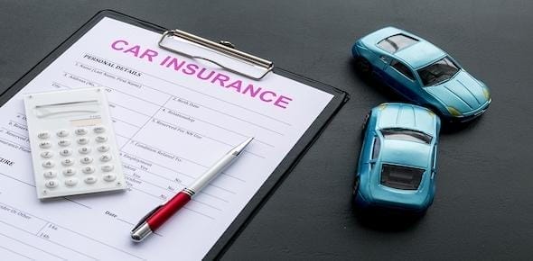 A car insurance form, accompanied by a pen and calculator, sits neatly on a gray surface alongside two blue toy cars. Ensure you're well-informed about your coverage to avoid mistakes.