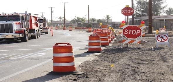Road with construction signs and orange barrels, indicating a stop for ongoing work. Stay alert to avoid work zone crashes and ensure safe navigation through this busy area.