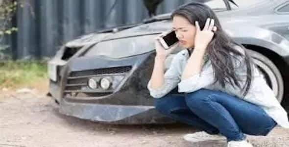 A woman is squatting beside a damaged car, talking on the phone and appearing distressed after a Michigan car accident.