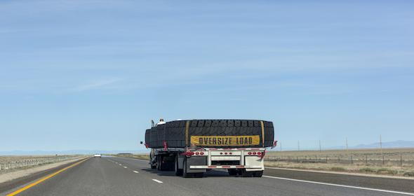 A truck marked with "Oversize Load" travels down the highway, carrying massive tires and drawing attention from all as it navigates the road.