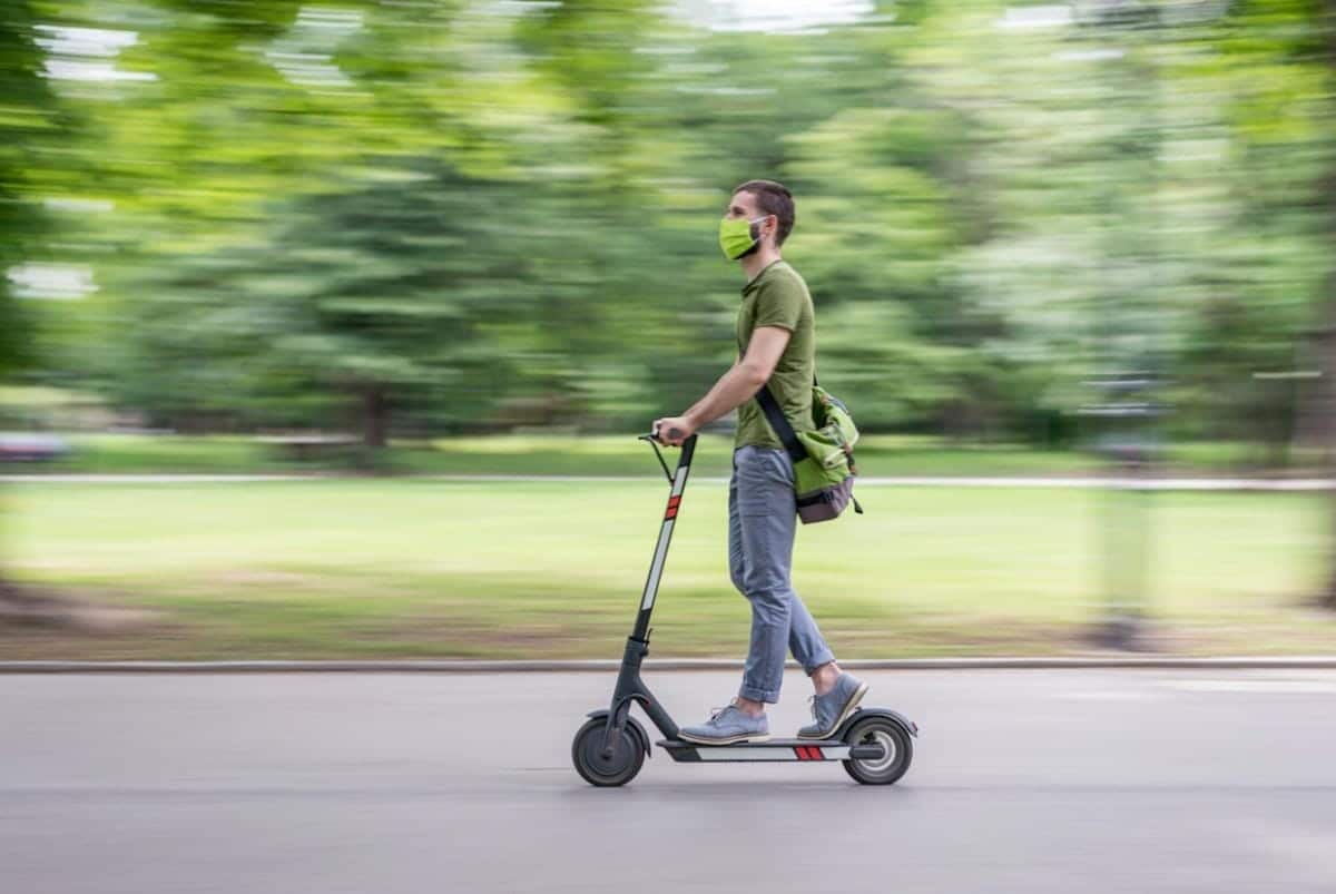 Wearing a green mask and shirt, the person skillfully navigates their Detroit electric scooter swiftly through the park, mindful of sidewalk safety.
