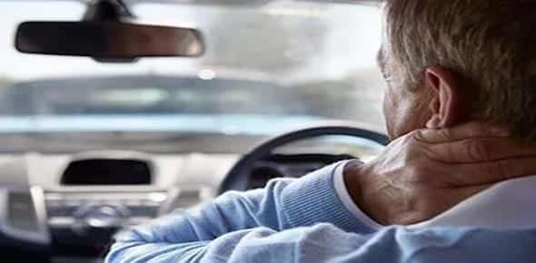 A person is sitting in a car, holding their neck with one hand, possibly experiencing discomfort from whiplash.