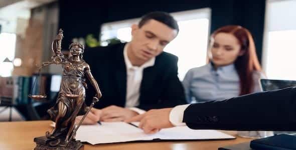 Two people are meticulously reviewing documents at a desk, with a small statue of Lady Justice symbolizing balance and fairness in the foreground, setting the tone for their personal injury mediation session.