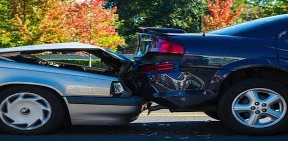 Two cars are involved in a rear-end collision on the road, with visible damage to the front of the silver car and the rear of the black car. Amidst trees in the background, questions swirl about who is at fault and whether a legal claim will follow.