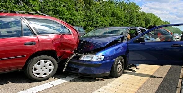 A blue car rear-ends a red car on a tree-lined road, causing visible damage from the car accident.