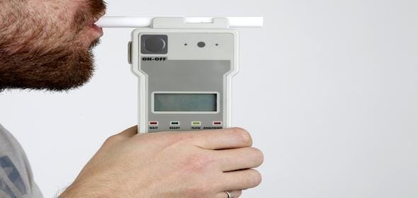 A person uses a breathalyzer, carefully holding the device with a mouthpiece inserted, ensuring accurate results after a truck accident potentially involving alcohol.