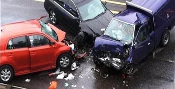 A three-car crash on a wet Michigan road involved a red car, black car, and purple truck with visible front-end damage. Debris was scattered around the vehicles.