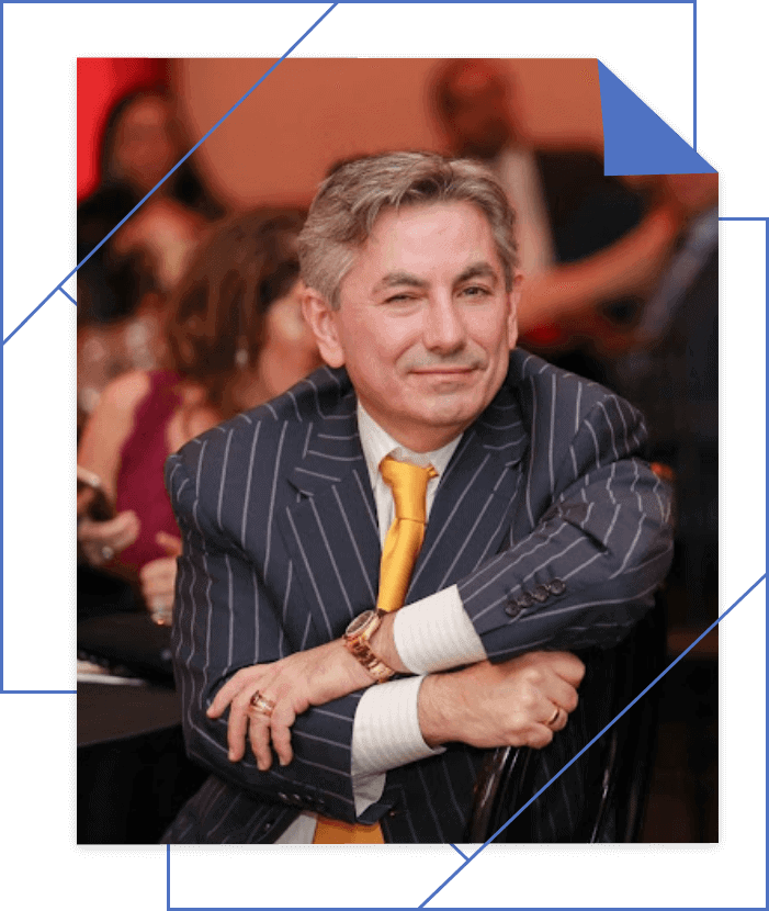 Joseph Dedvukaj in a pinstriped suit and yellow tie sits with folded arms, smiling at an event.