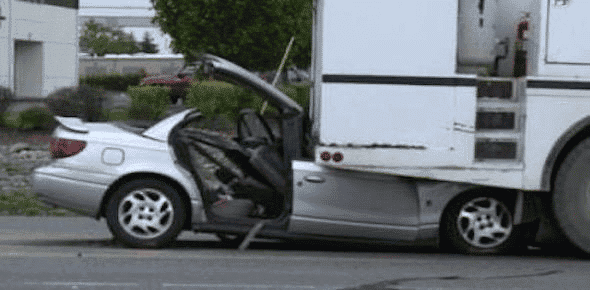 A silver car is partially lodged under the rear of a large white truck on a street, with significant front-end damage visible from the accident, highlighting the severity of the car underride incident.