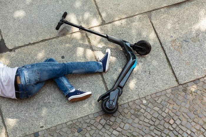 A person is lying on a Michigan sidewalk next to a fallen scooter, pondering the rules of the road.
