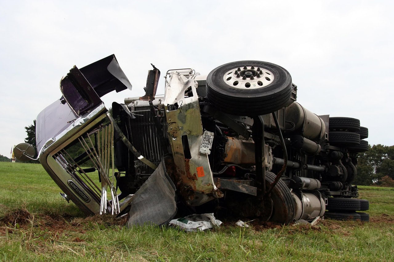 An overturned semi-truck lies on its side in a grassy field, showing significant damage to the cabin and trailer. If you find yourself in such a situation, knowledgeable Semi Truck Accident attorneys can provide invaluable assistance.