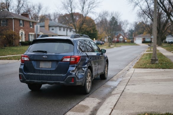 Dark SUV with a deeply dented rear quarter panel parked on an empty street after a hit and run